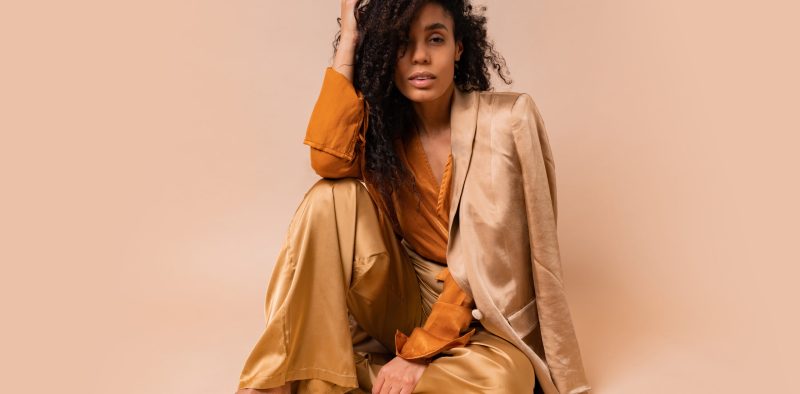 Stunning  african model with voluminous curly hairstyle in elegant   costume posing in studio on beige background.